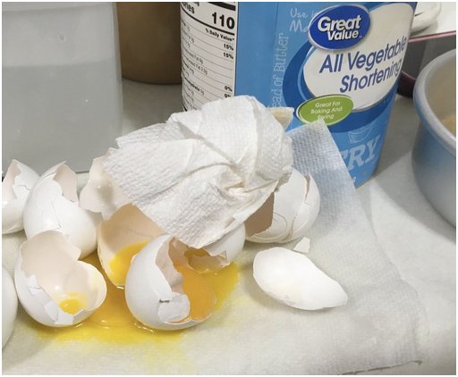 a mess of broken eggs and sticky paper towels next to a can of Crisco and a cake pan